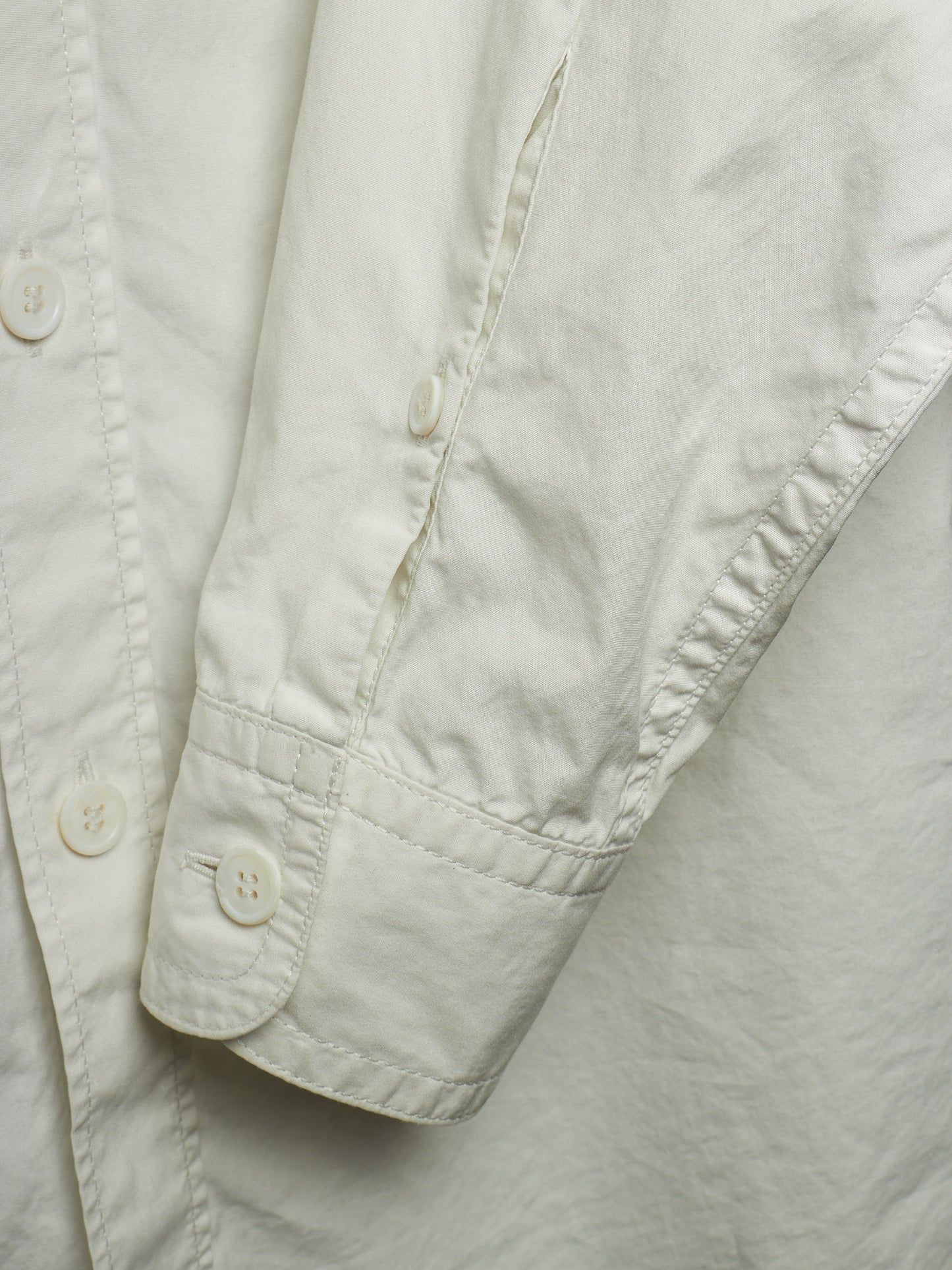 Close-up detail of a light cream or off-white button-up shirt, showing the sleeve cuff with a button and the fabric texture.