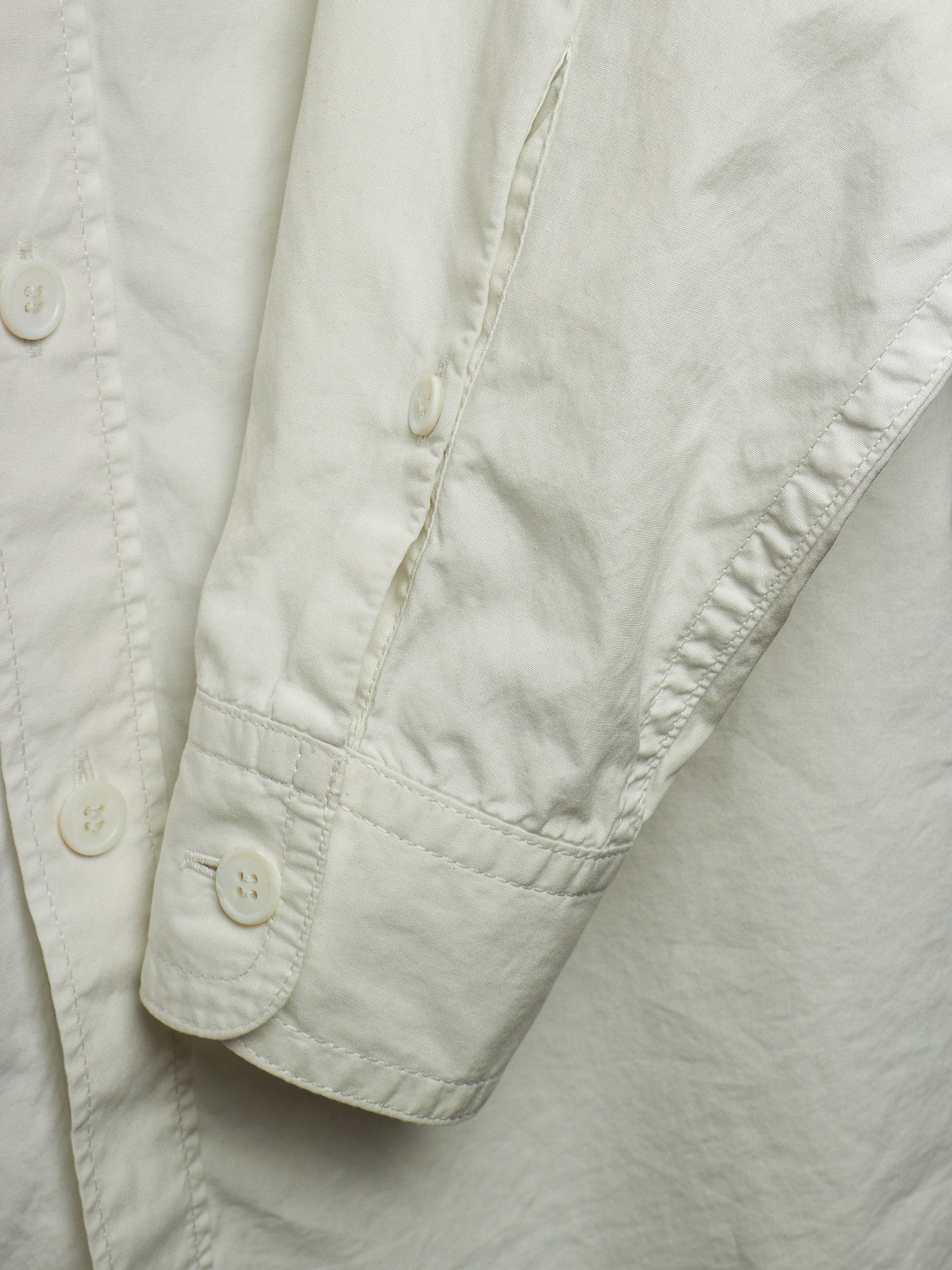 Close-up detail of a light cream or off-white button-up shirt, showing the sleeve cuff with a button and the fabric texture.