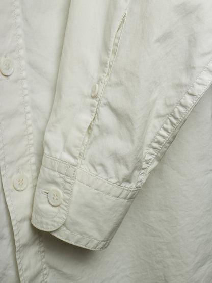 Close-up detail of a light cream or off-white button-up shirt, showing the sleeve cuff with a button and the fabric texture.