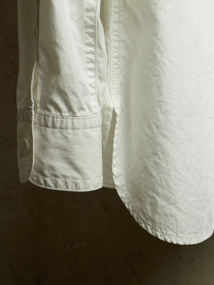 Close-up detail of an off-white linen shirt sleeve with a buttoned cuff and visible fabric texture, set against a dark brown background.