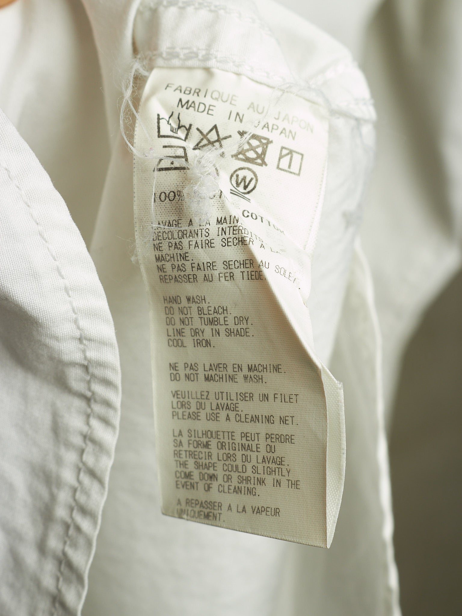 A close-up of a white garment's interior label showing 'Made in Japan' and care instructions in French and English.
