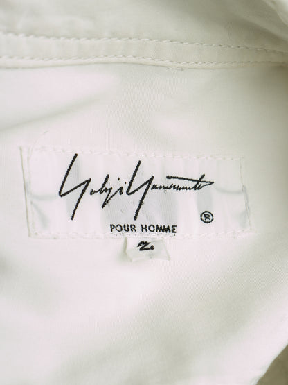 Close-up of a white garment's inner neck label featuring the black script logo 'Yoshida Yamamoto' and 'POUR HOMME' printed below it.