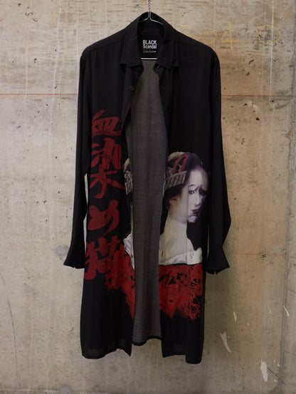 Black shirt with graphic design on a hanger against a textured wall.