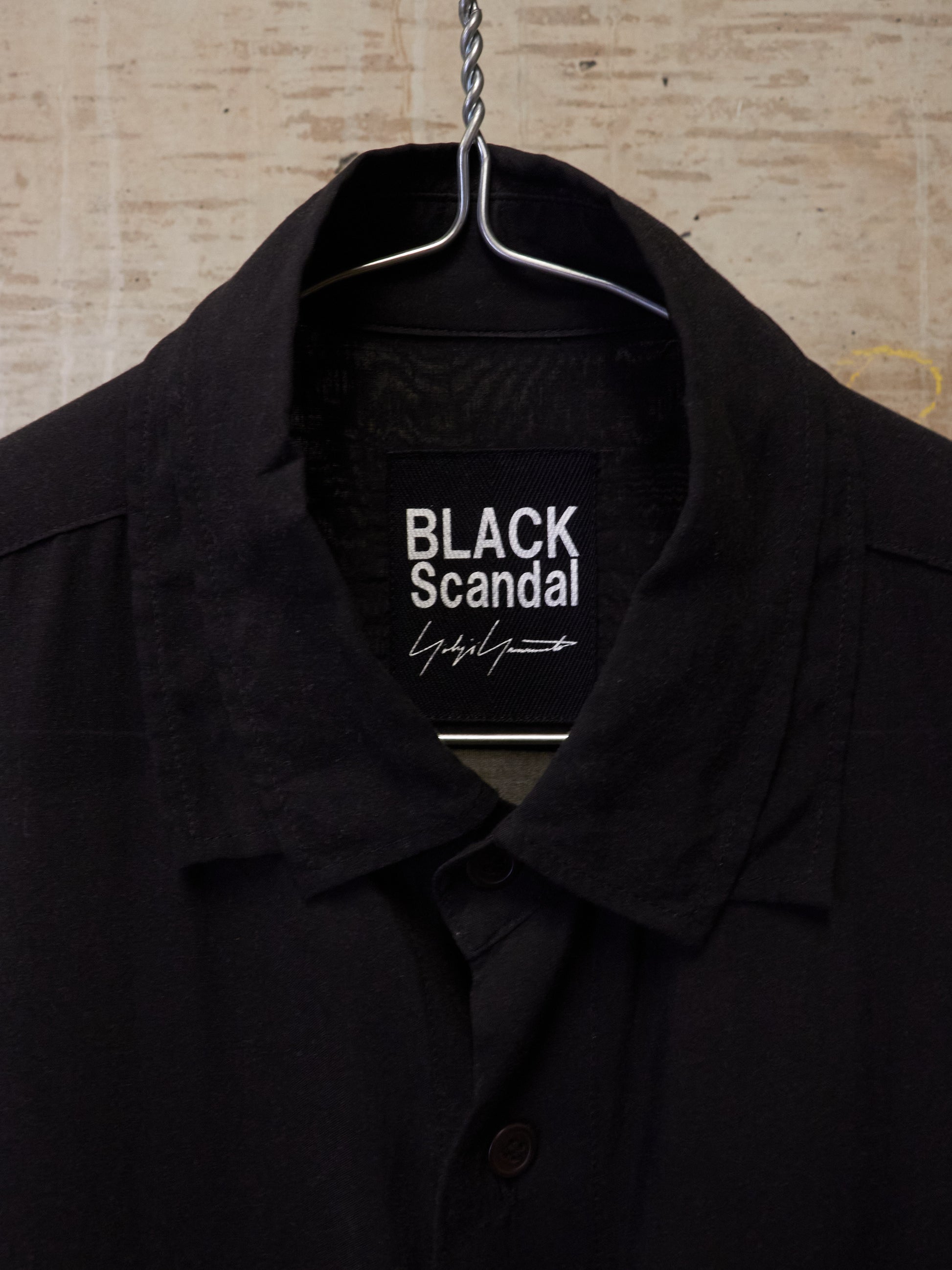 Black coat on a hanger with 'BLACK Scandal' label against a textured beige background