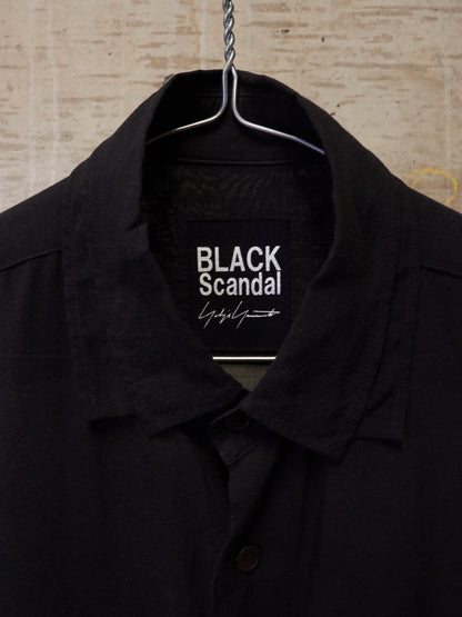 Black coat on a hanger with 'BLACK Scandal' label against a textured beige background