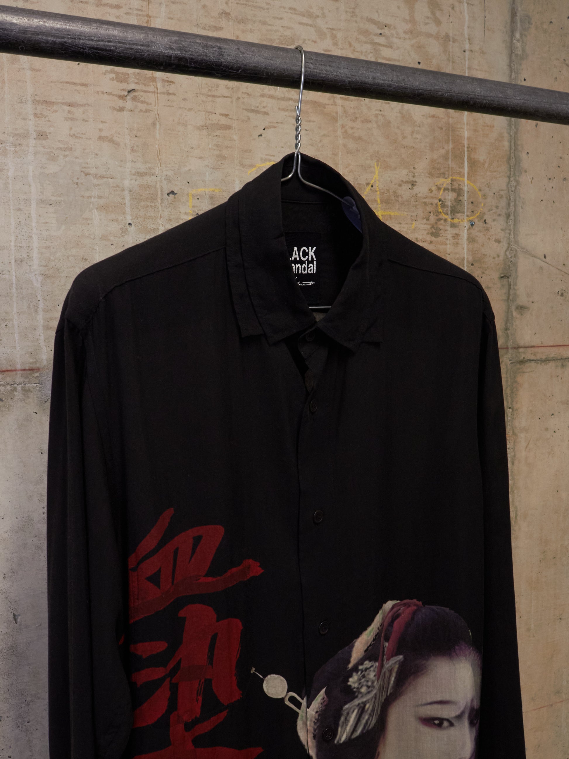 Black shirt with red text and a graphic of a person hanging on a rack against a concrete wall.