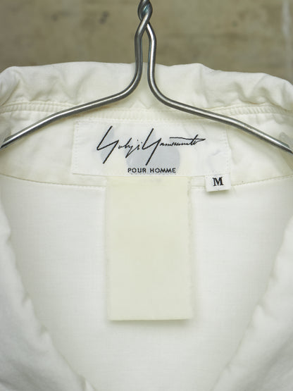 Close-up of the inside neck of a white or off-white jacket hanging on a silver metal hanger. The inner label reads 'Gucci' in script with 'Pour Homme' underneath and a small size tag marked 'M'.