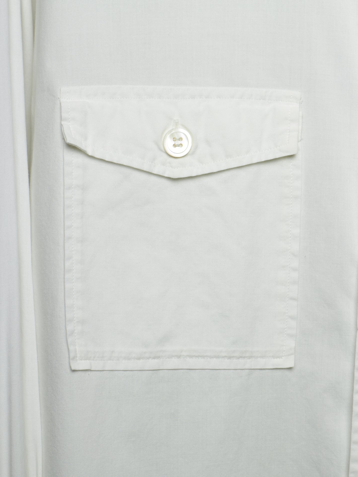 Close-up of a white button-up shirt featuring a single front flap pocket with a white button closure.