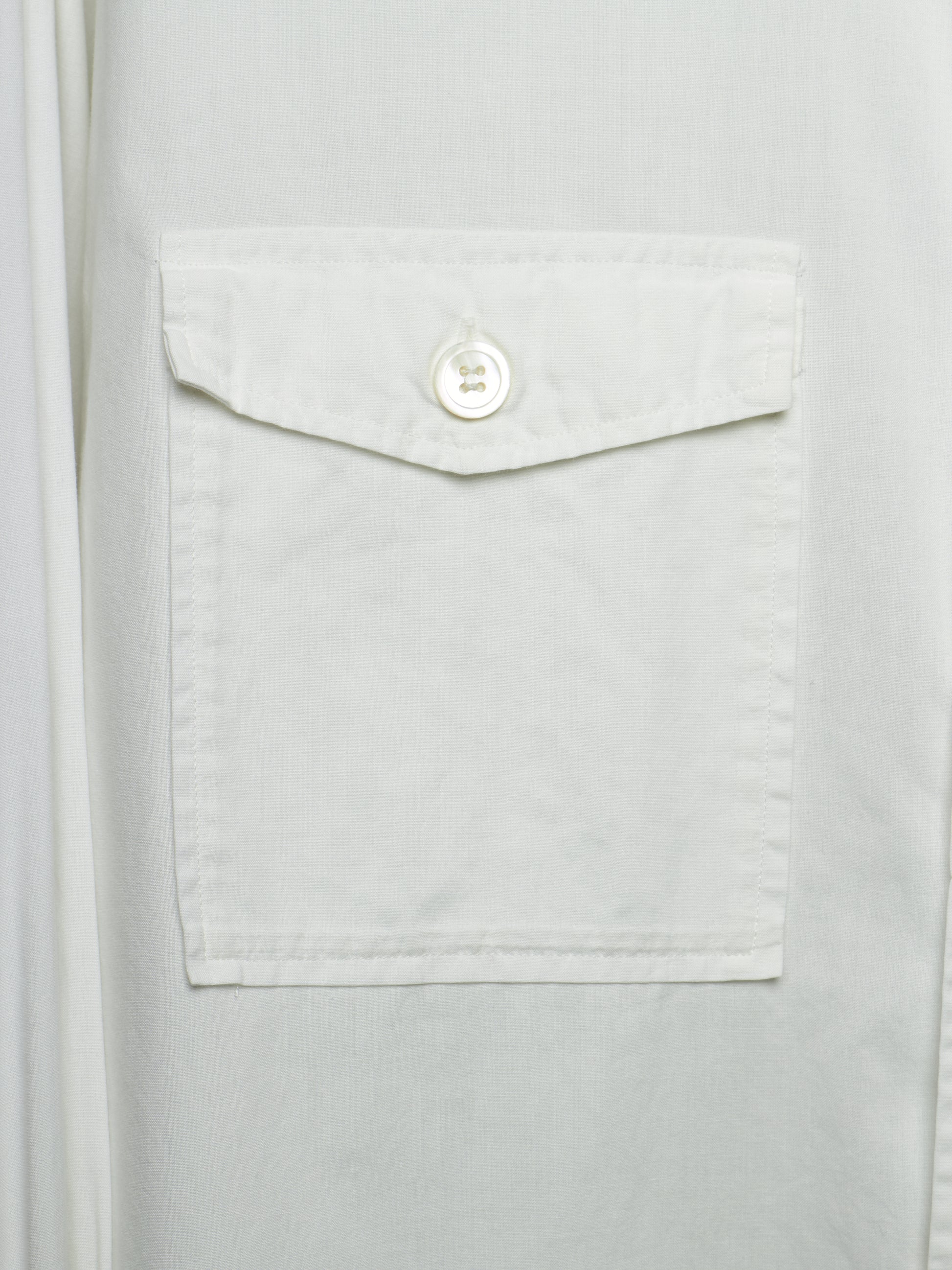Close-up of a white button-up shirt featuring a single front flap pocket with a white button closure.