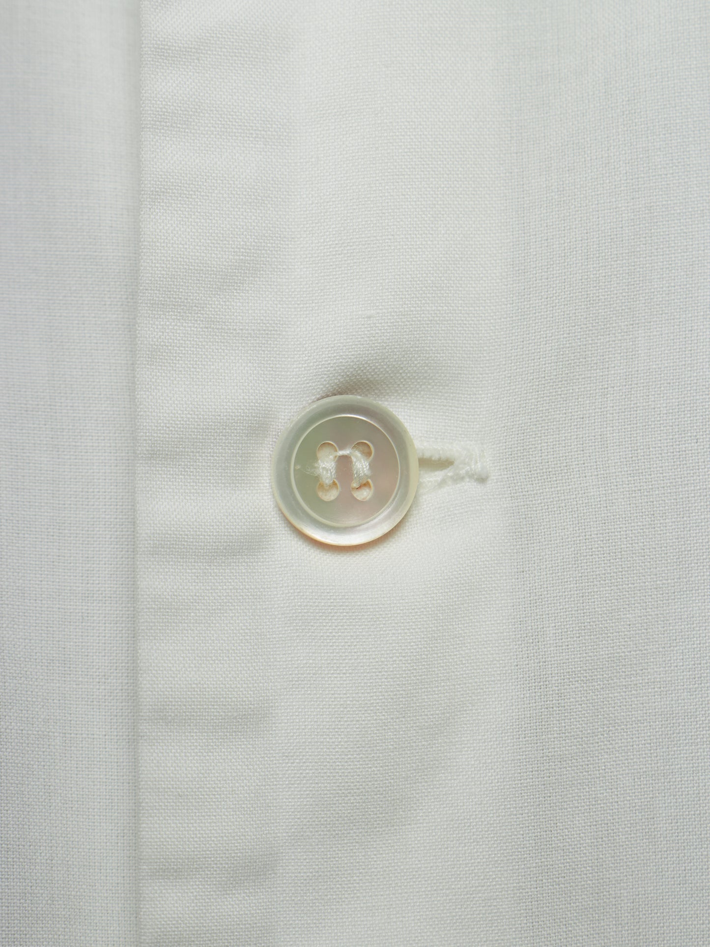 Close-up of a white textured fabric with a single round translucent button on the left side of a vertical seam.