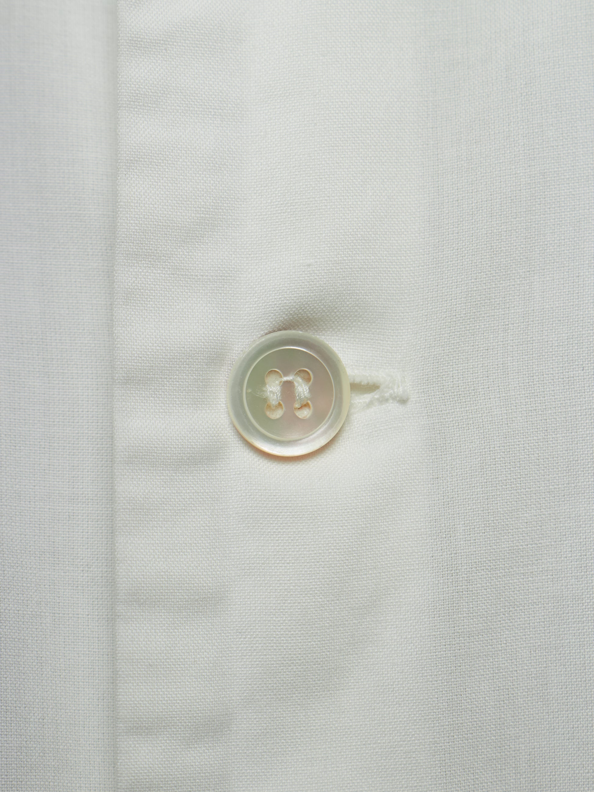 Close-up of a white textured fabric with a single round translucent button on the left side of a vertical seam.