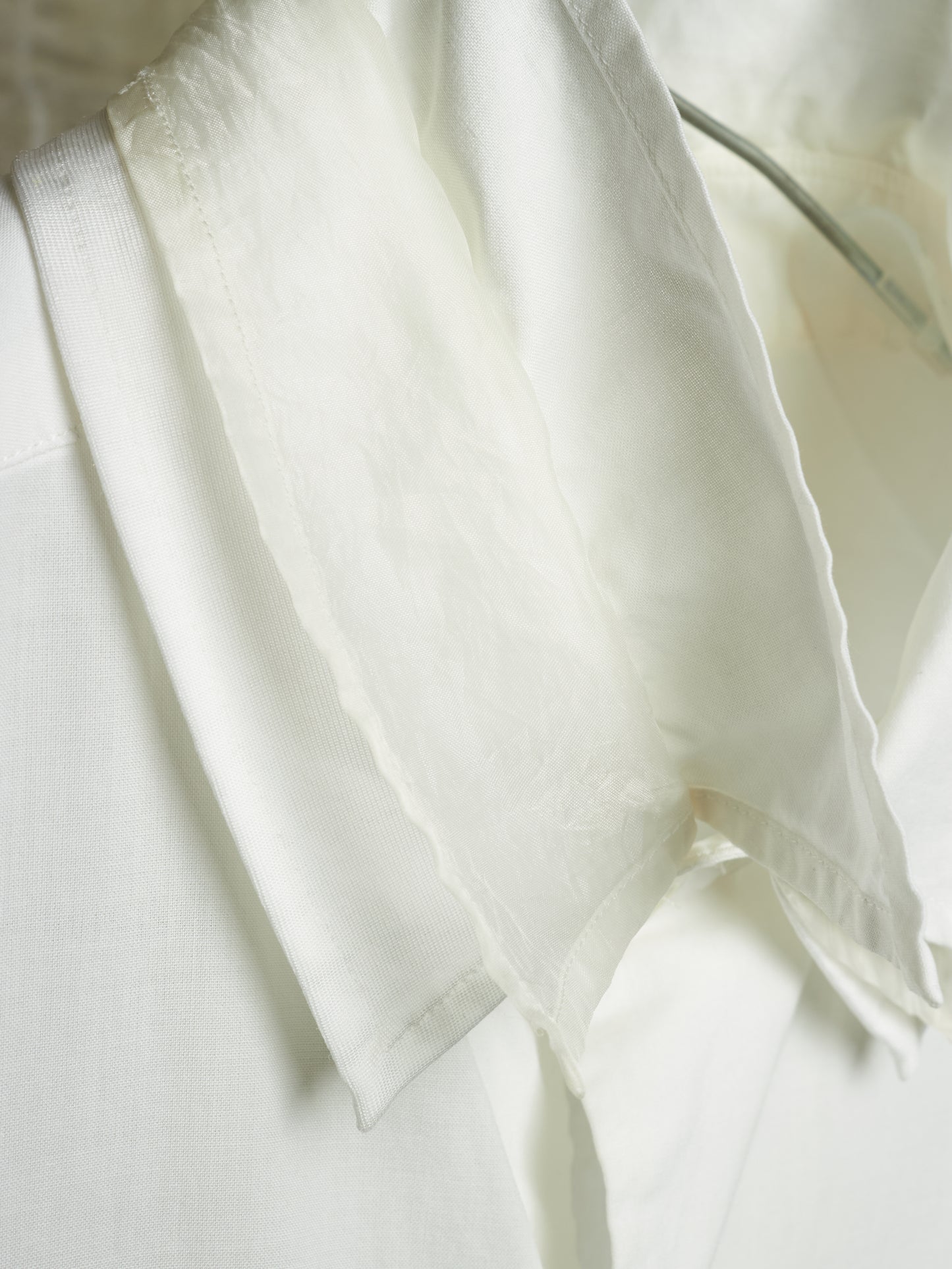 A close-up of a white lightweight fabric garment or textile draped over a white structured surface, showing soft folds and a slightly sheer texture.