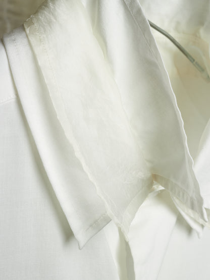A close-up of a white lightweight fabric garment or textile draped over a white structured surface, showing soft folds and a slightly sheer texture.