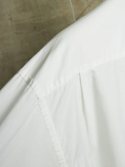 Close-up detail of a white shirt or garment fabric with visible seams and a neutral concrete-textured background.