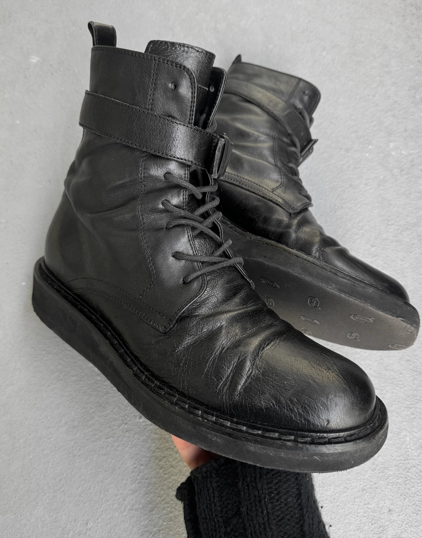 Black leather boots with a strap on a gray background