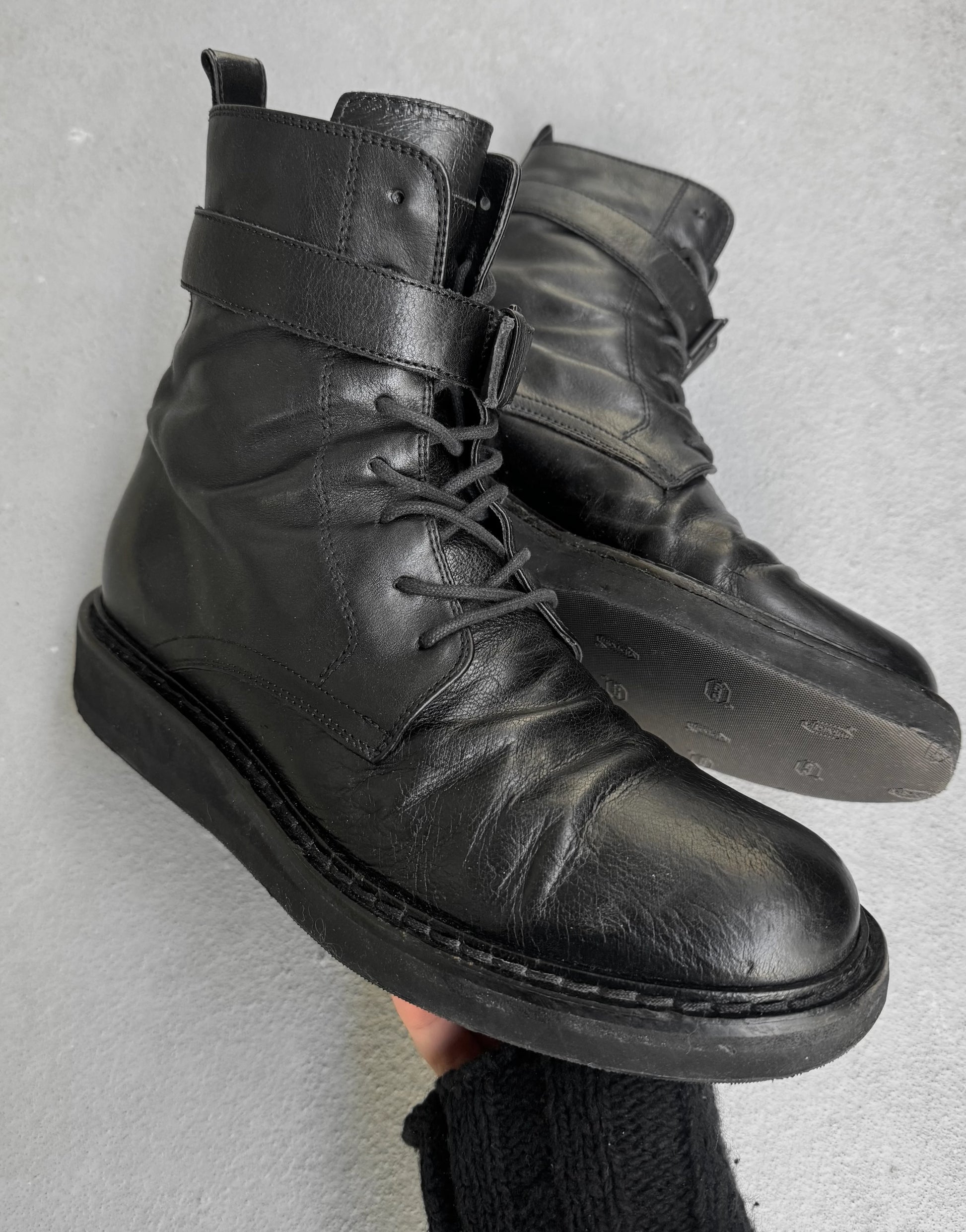 Black leather boots with a strap on a gray background