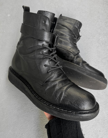 Black leather boots with a strap on a gray background