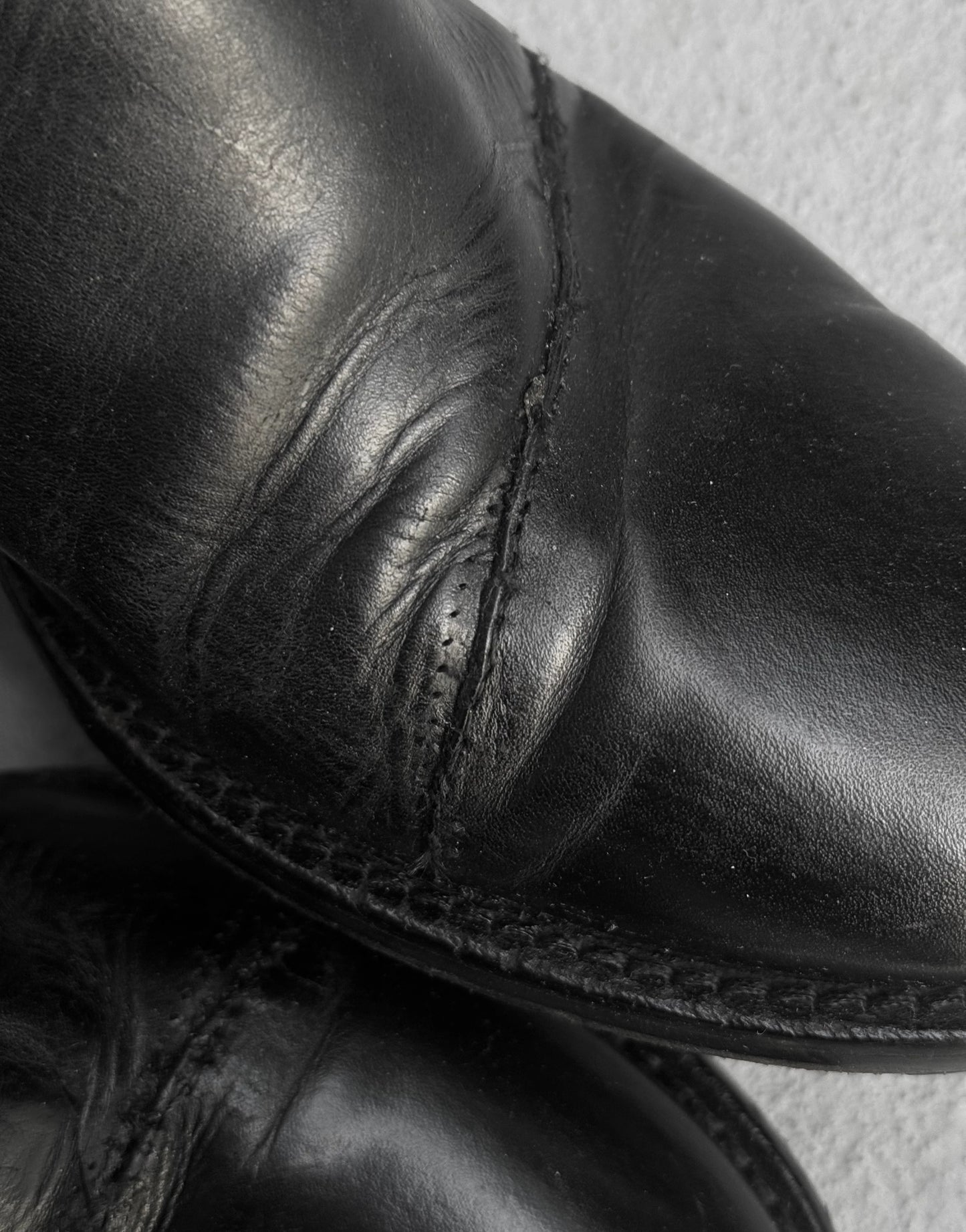 Close-up of a black leather boot with detailed stitching on a white background