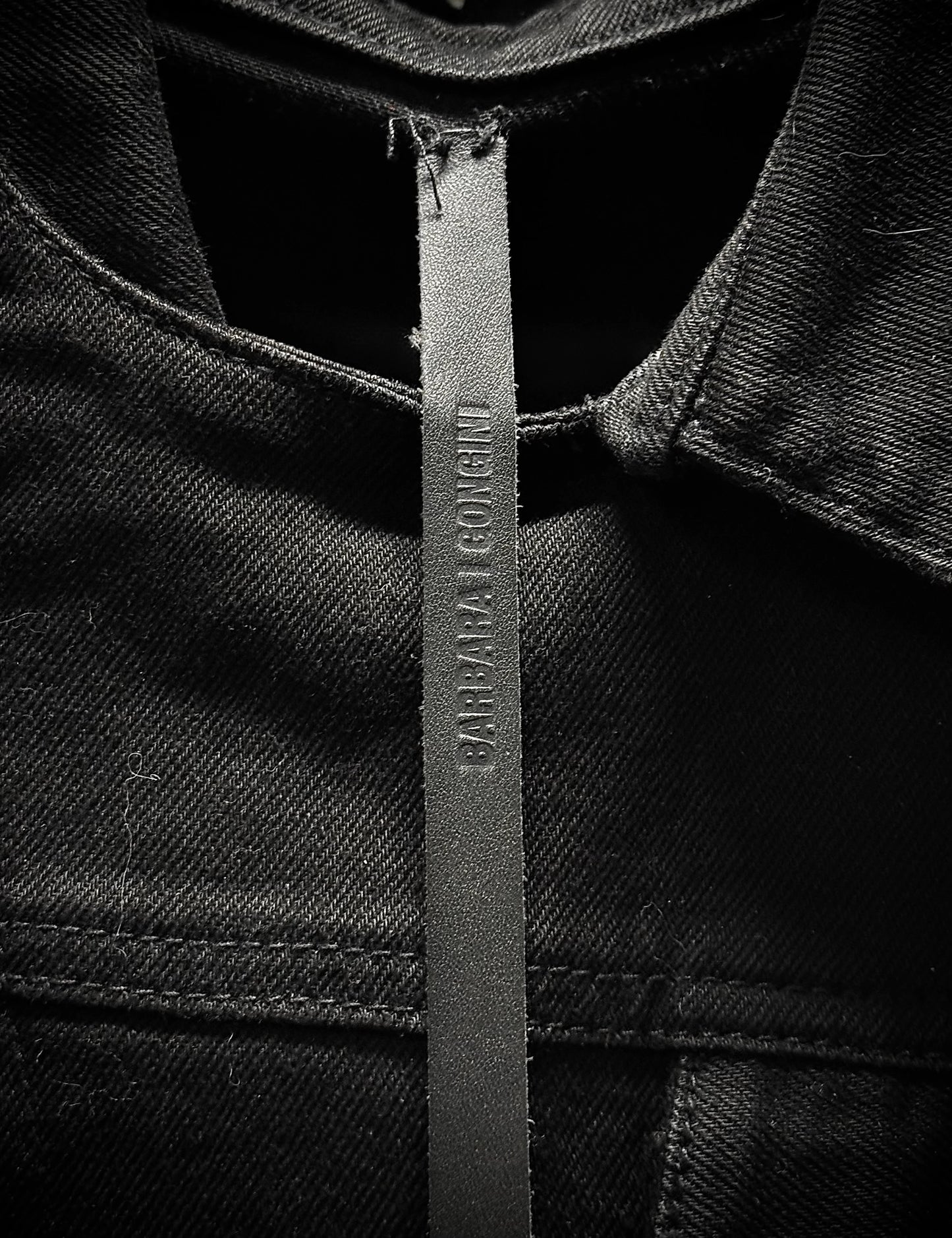 Close-up of a black denim jacket with a brand label on a dark background