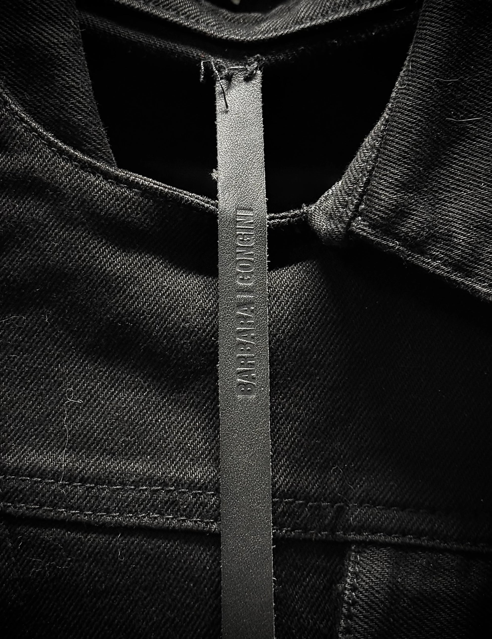 Close-up of a black denim jacket with a brand label on a dark background
