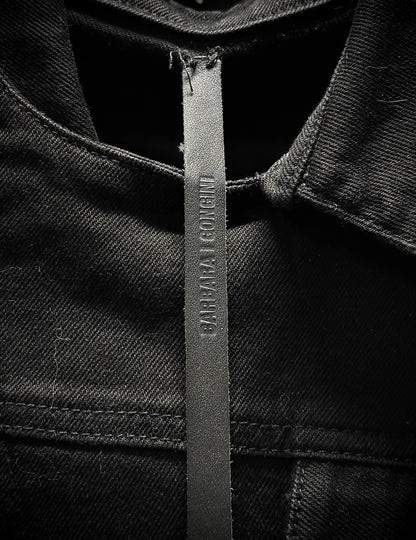 Close-up of a black denim jacket with a brand label on a dark background