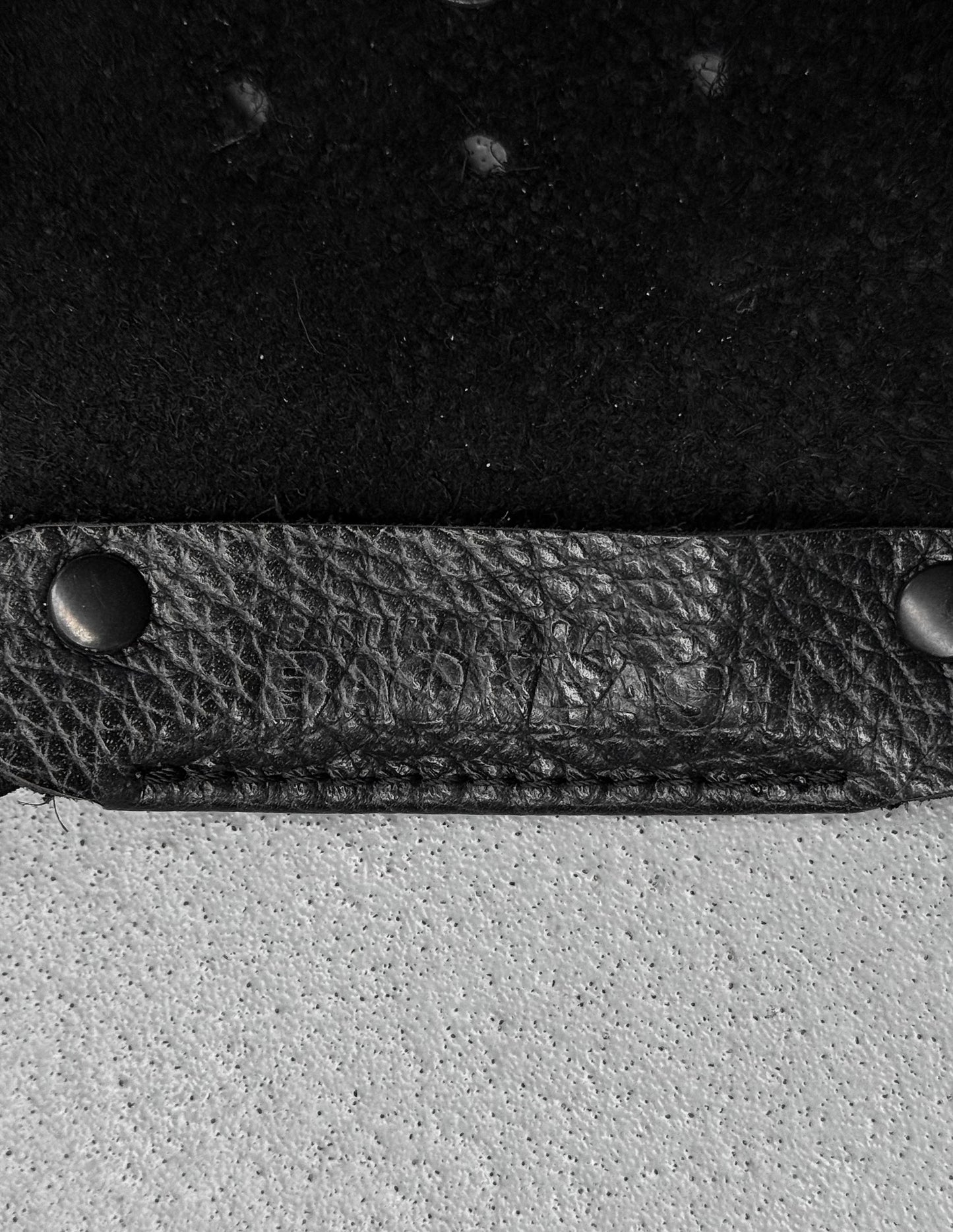 Close-up of a black leather strap with metal fasteners on a textured surface.