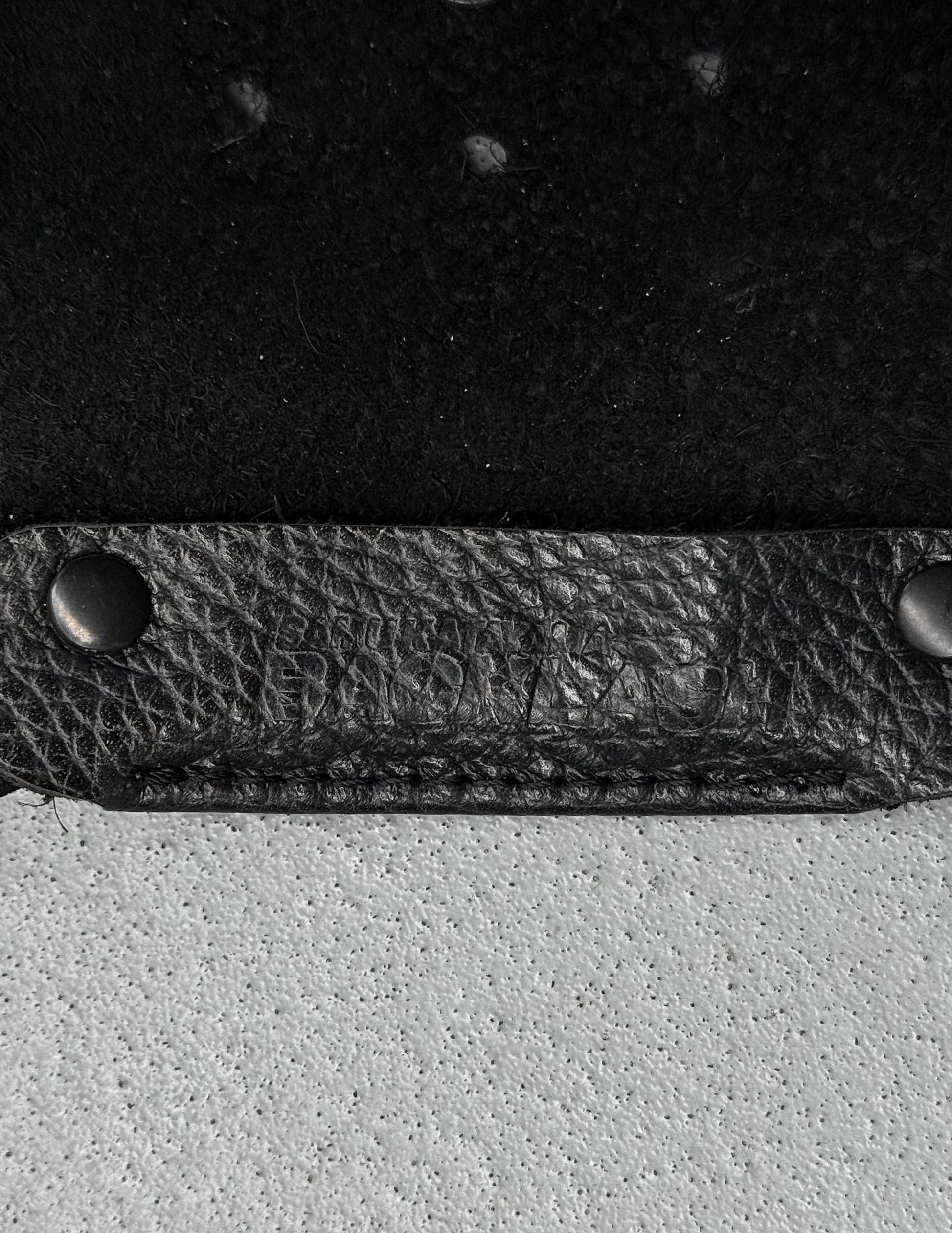 Close-up of a black leather strap with metal fasteners on a textured surface.