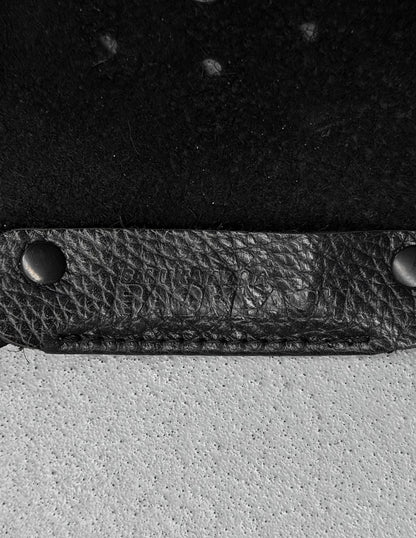 Close-up of a black leather strap with metal fasteners on a textured surface.