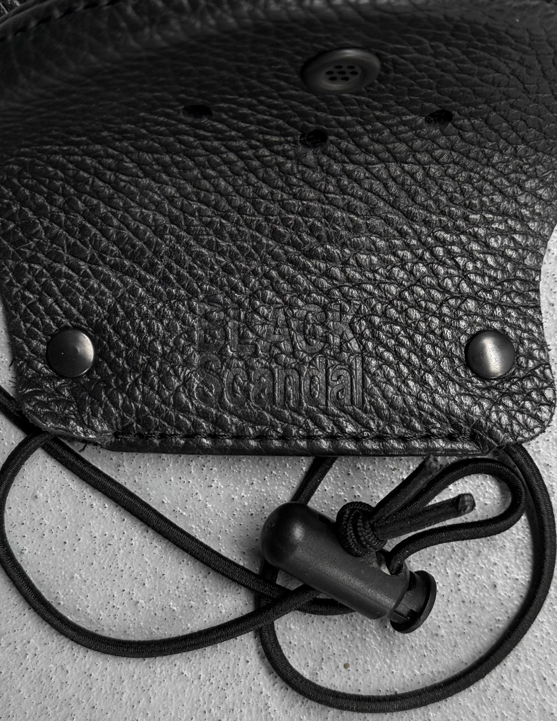 Black leather pouch with a strap on a textured surface