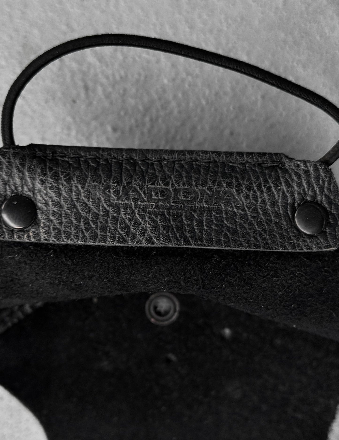 Close-up of a textured black leather strap with metal fasteners on a light gray background