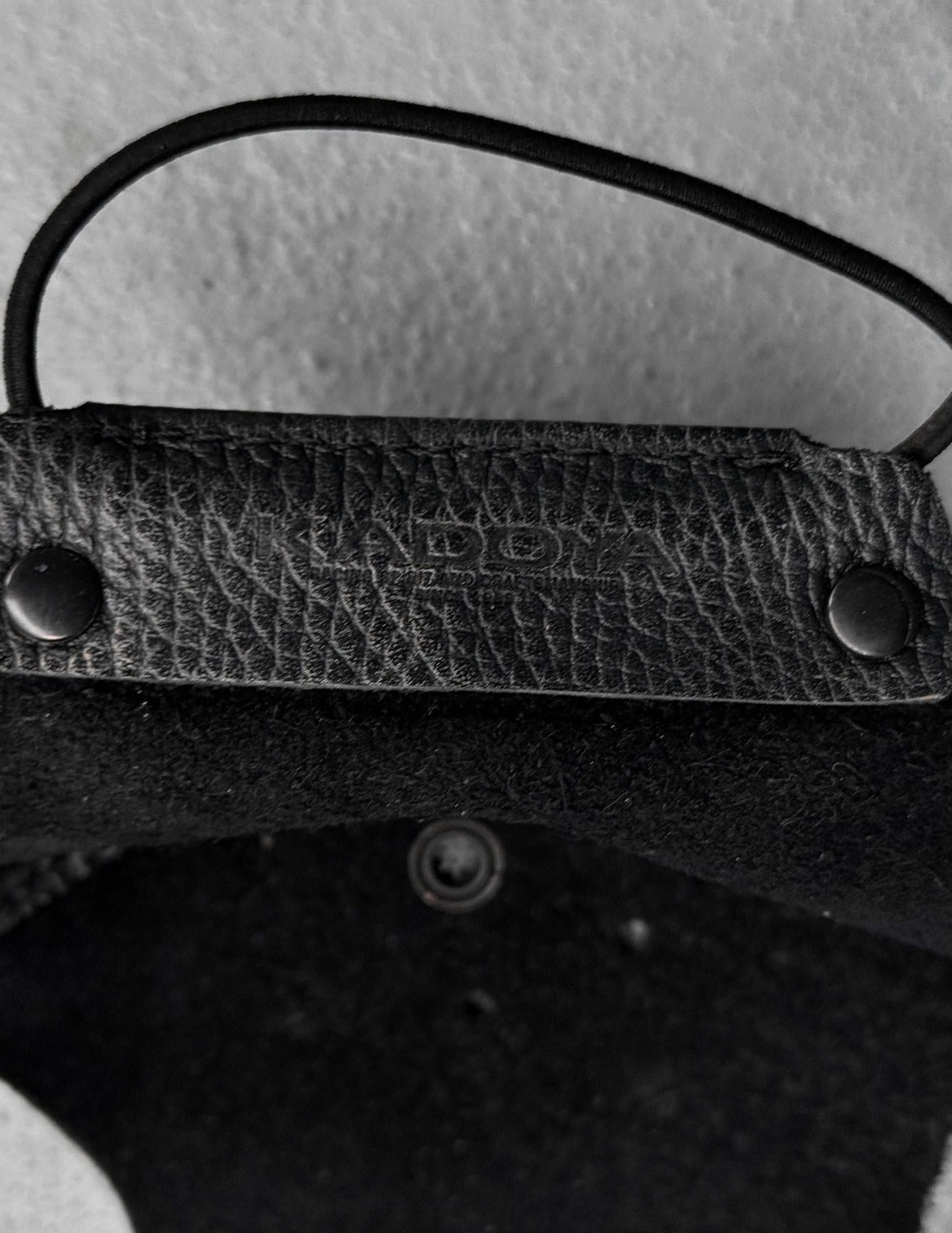 Close-up of a textured black leather strap with metal fasteners on a light gray background