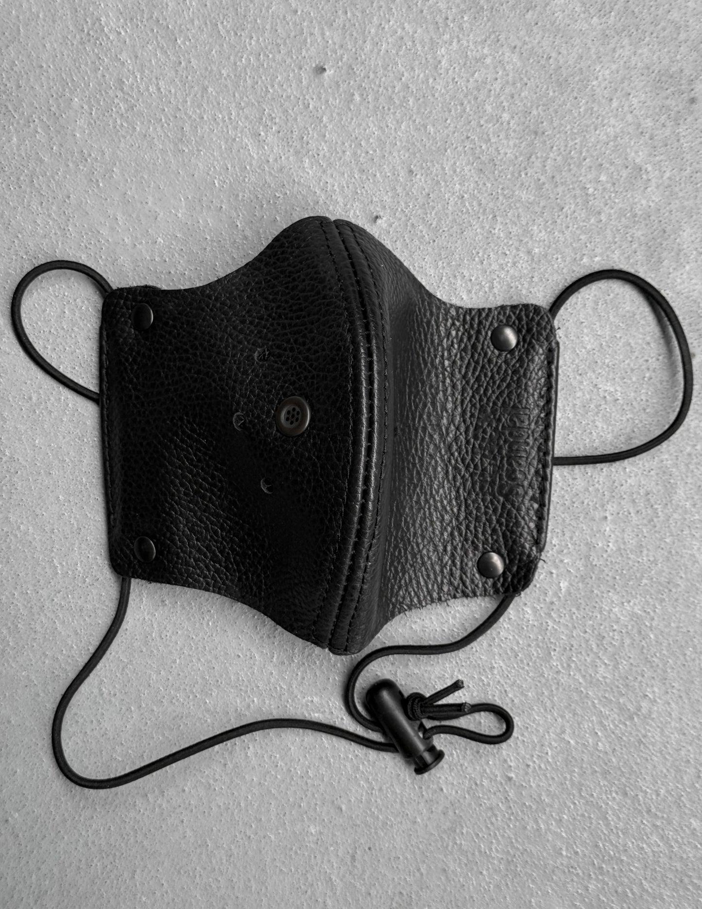 Black leather face mask with straps on a gray background