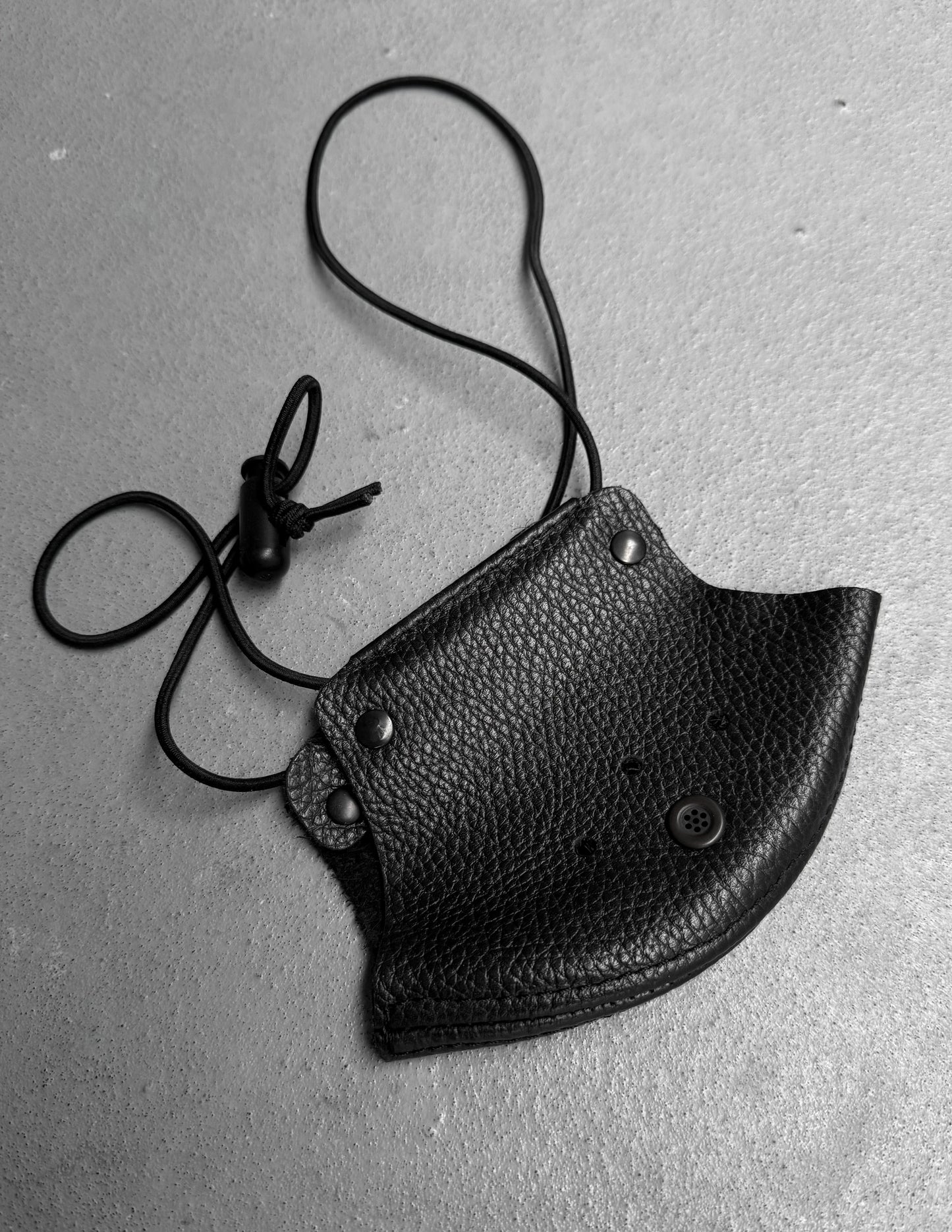 Black leather pouch with a strap on a gray surface