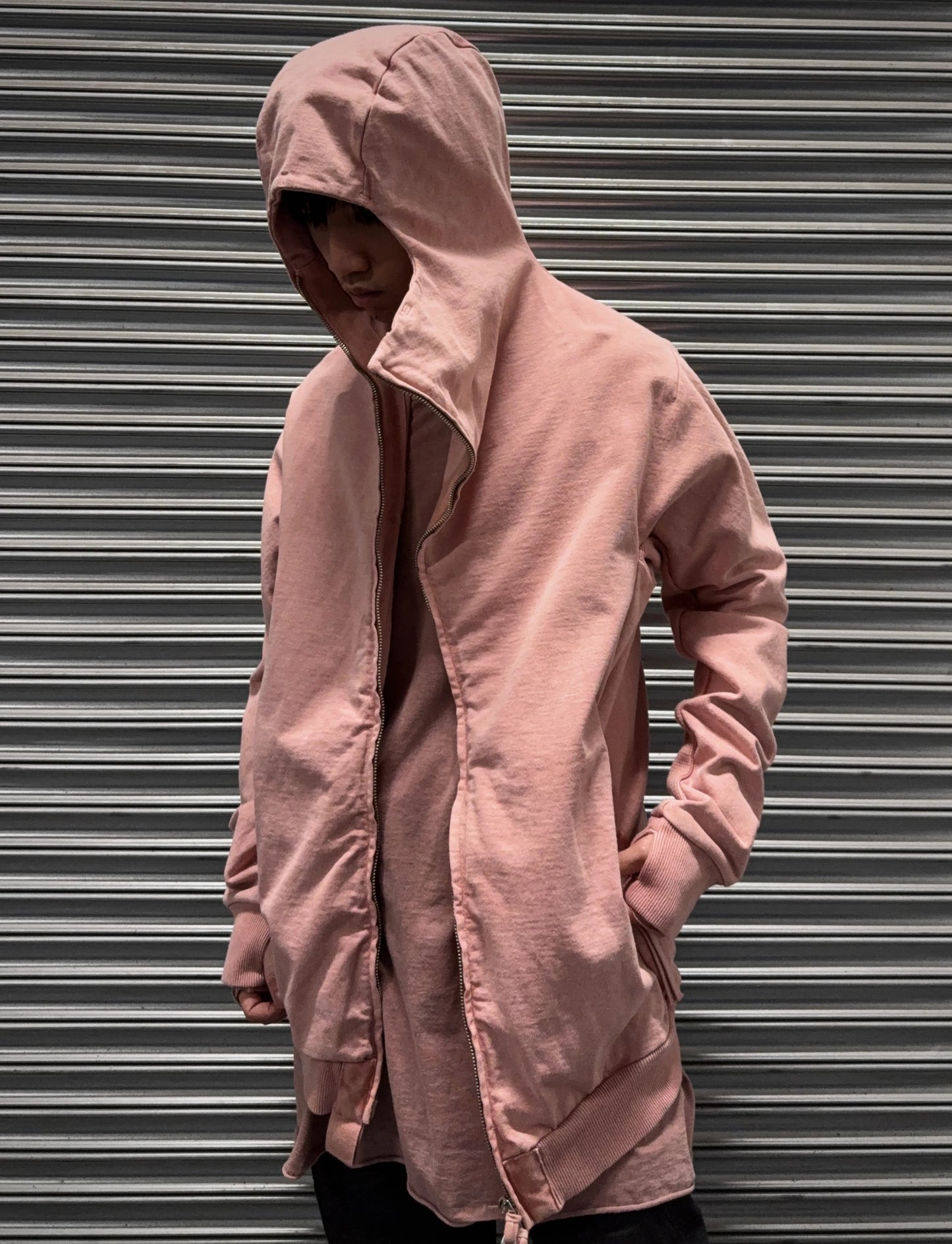 Person wearing a pink hooded jacket against a metallic shutter background