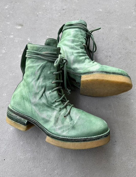 Pair of green suede boots with brown soles on a gray surface