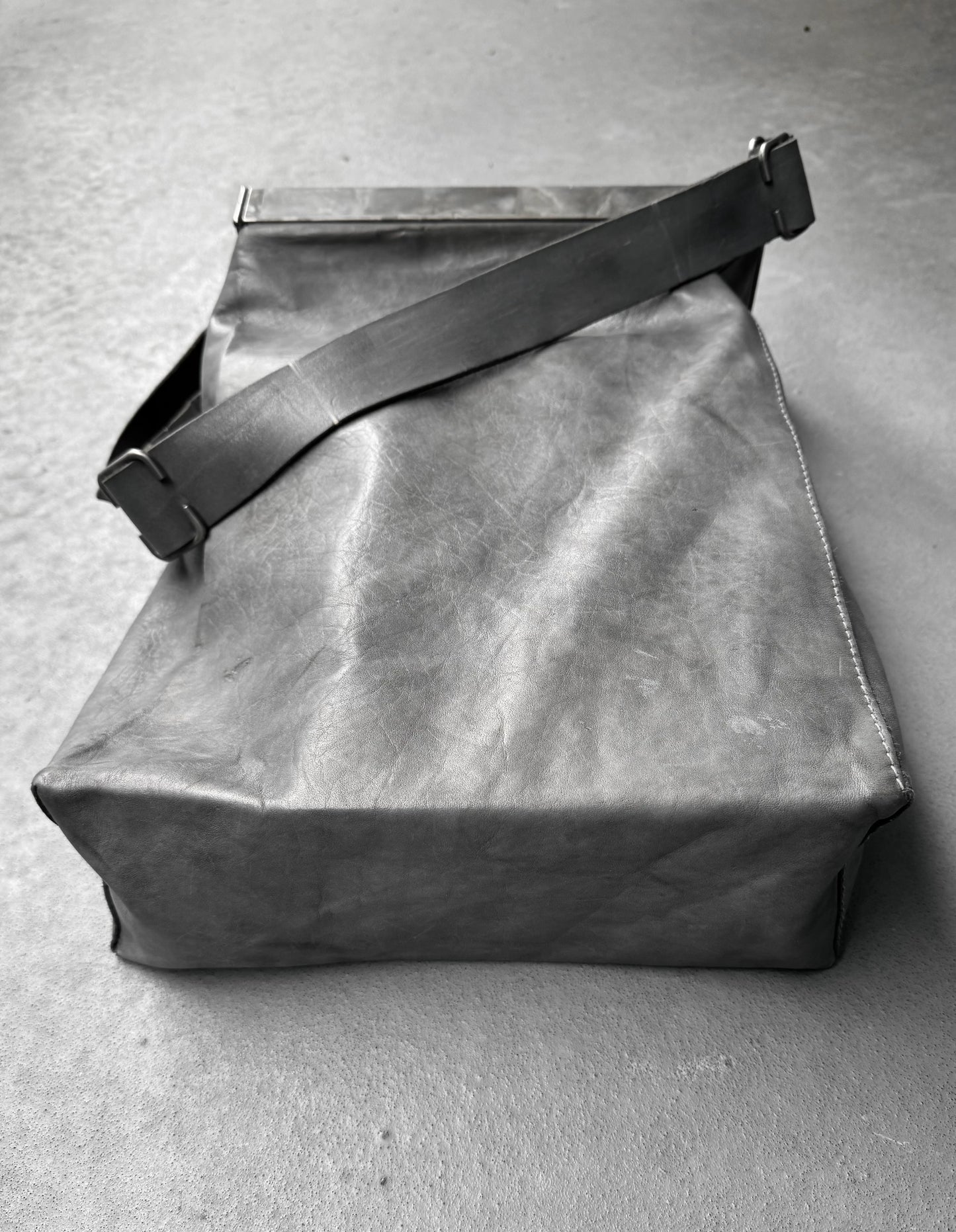 Gray leather bag with a strap on a gray concrete surface