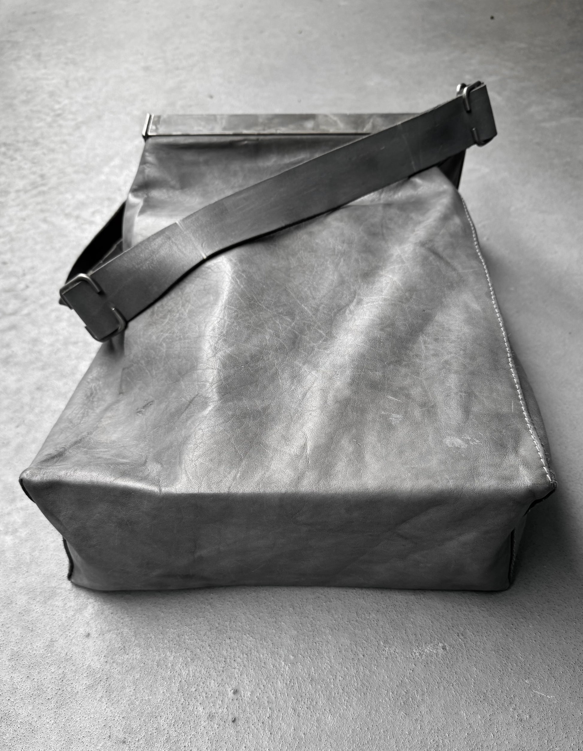 Gray leather bag with a strap on a gray concrete surface
