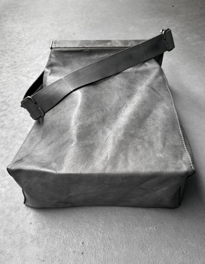 Gray leather bag with a strap on a gray concrete surface