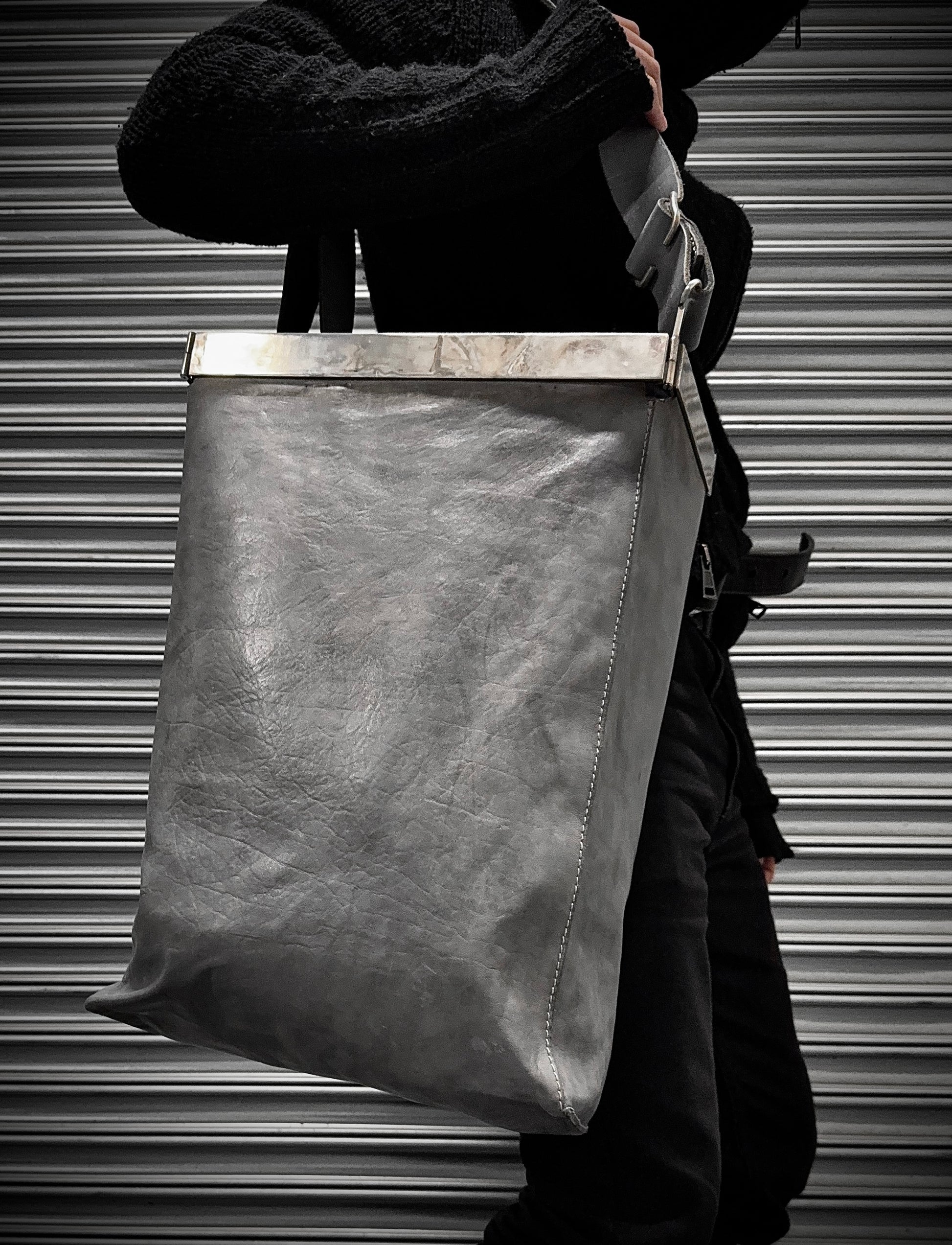 Person holding a large leather bag against a metallic shutter background