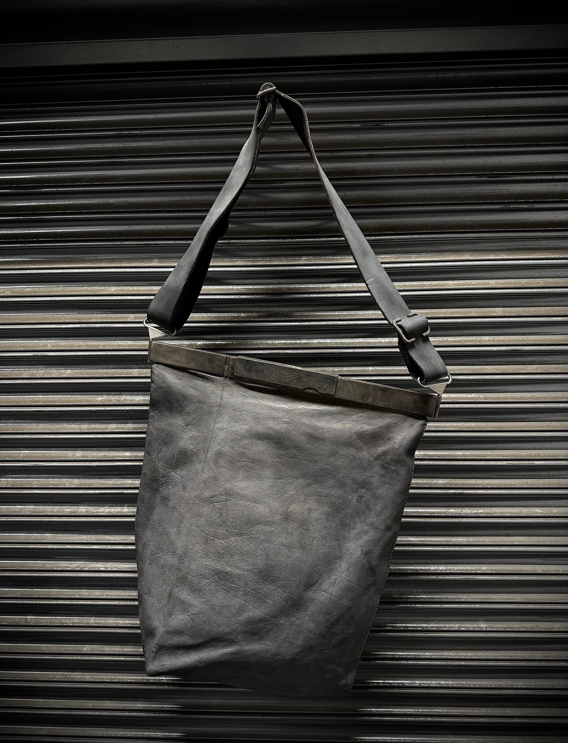 Dark gray leather tote bag with a strap against a metallic background