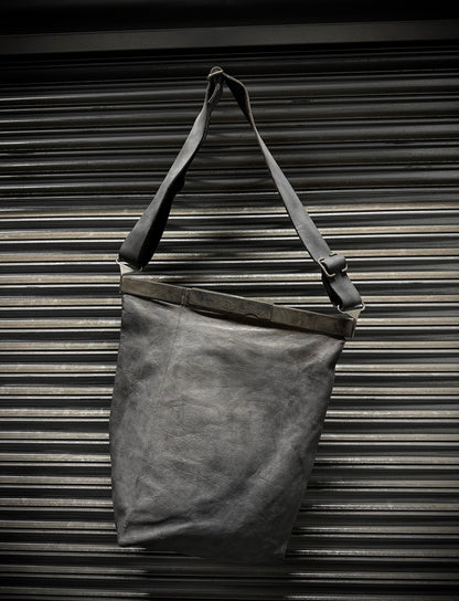 Dark gray leather tote bag with a strap against a metallic background