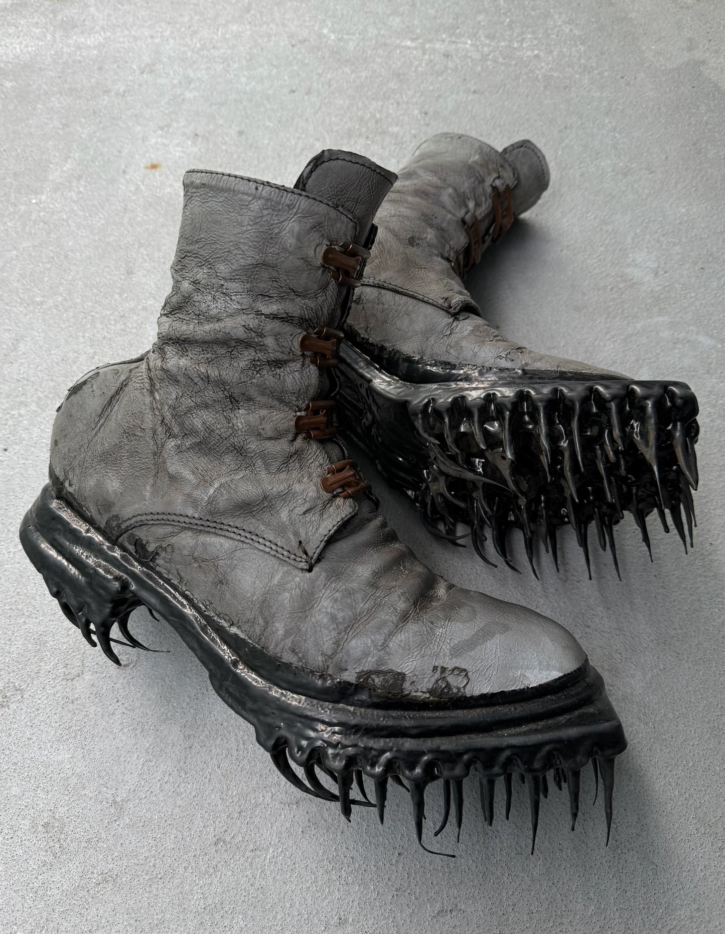 Pair of worn boots with spiked soles on a gray background