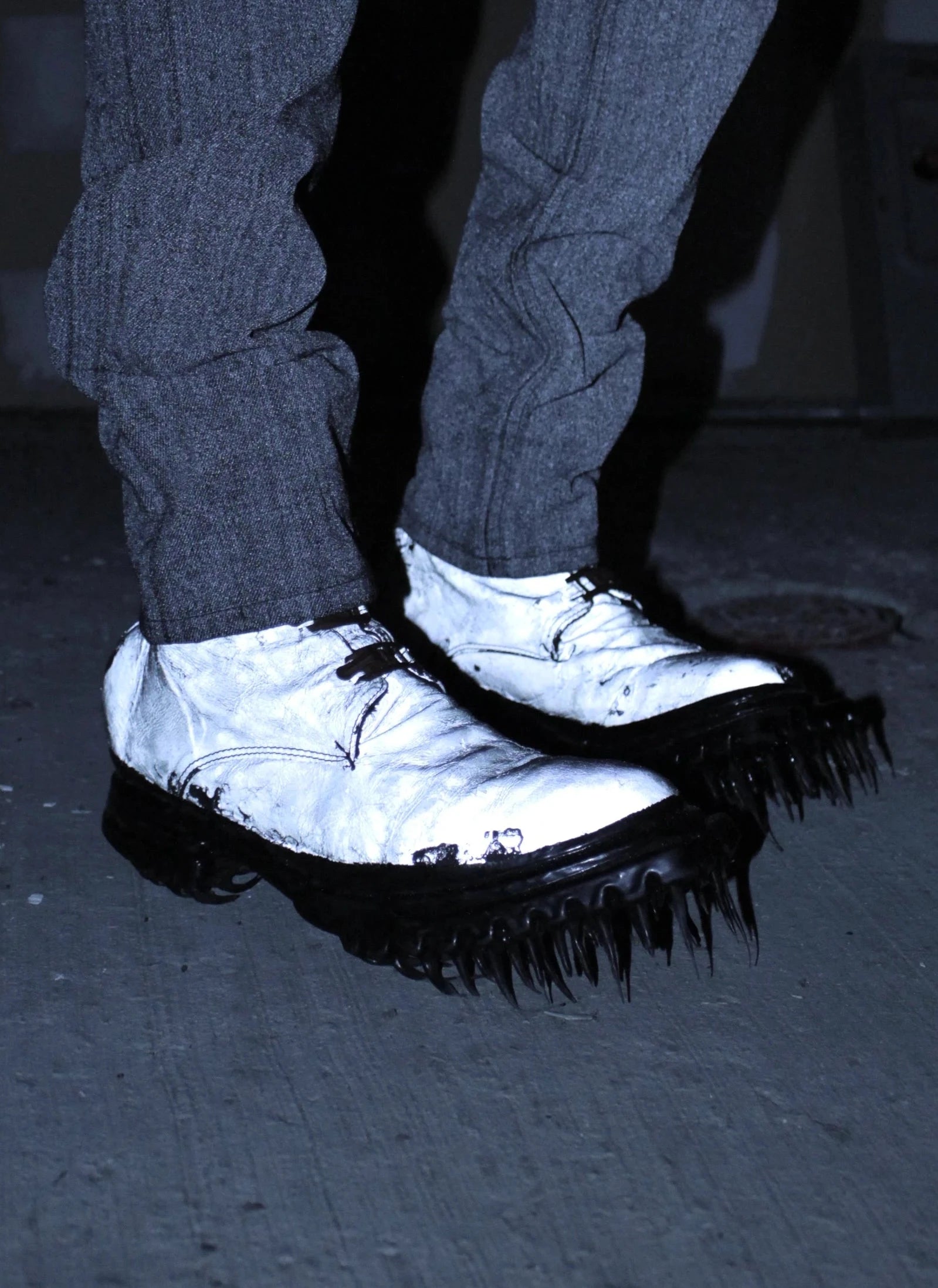 Person wearing dark pants and white shoes with black soles on a dark floor.