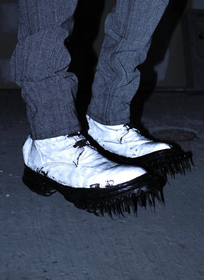 Person wearing dark pants and white shoes with black soles on a dark floor.