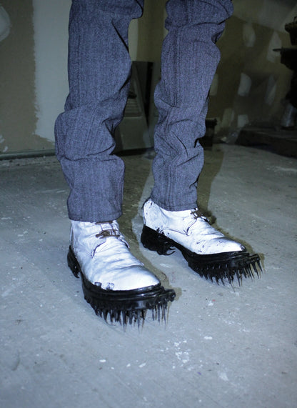 Person wearing white shoes with black spikes on a concrete floor.
