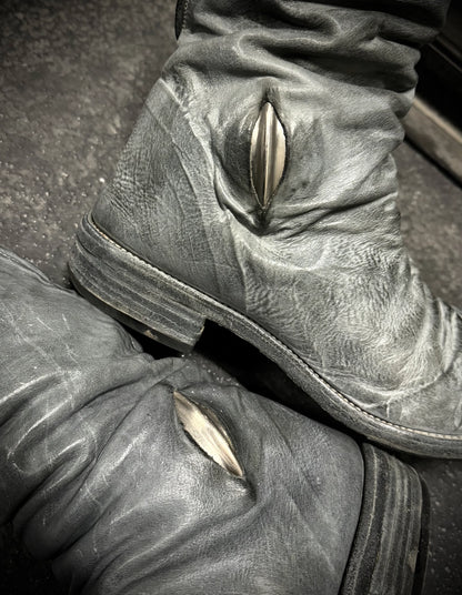 Close-up of worn leather boots with metal eyelets on a textured surface