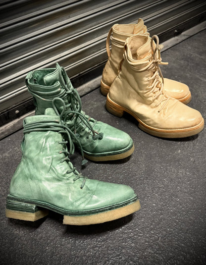 Pair of green and beige boots on a dark surface with a metallic background
