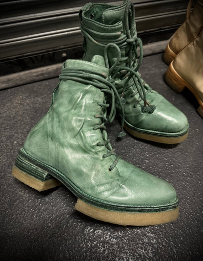 Green leather boots with beige soles on a dark surface