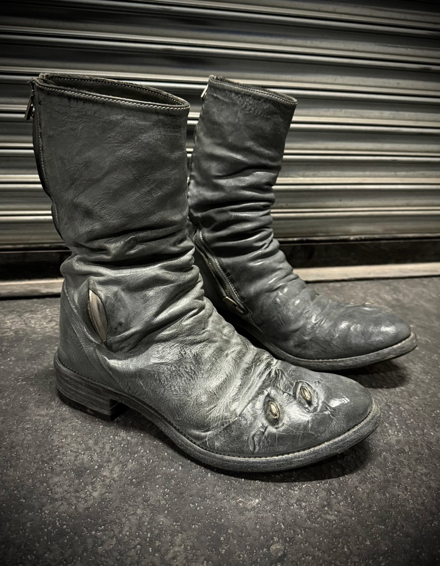 Pair of worn leather boots on a dark surface with a metallic background