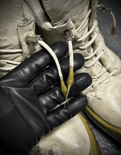 Close-up of a black glove holding a white cord against a textured beige background